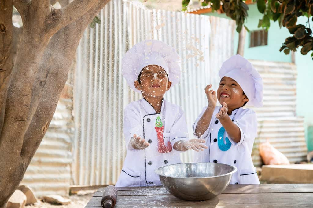 Two young boys in Bolivia are dressed in chef outfits and tossing flour into the air.