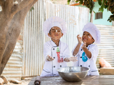 Two twin boys in Bolivia are wearing chef outfits and tossing flour into the air.