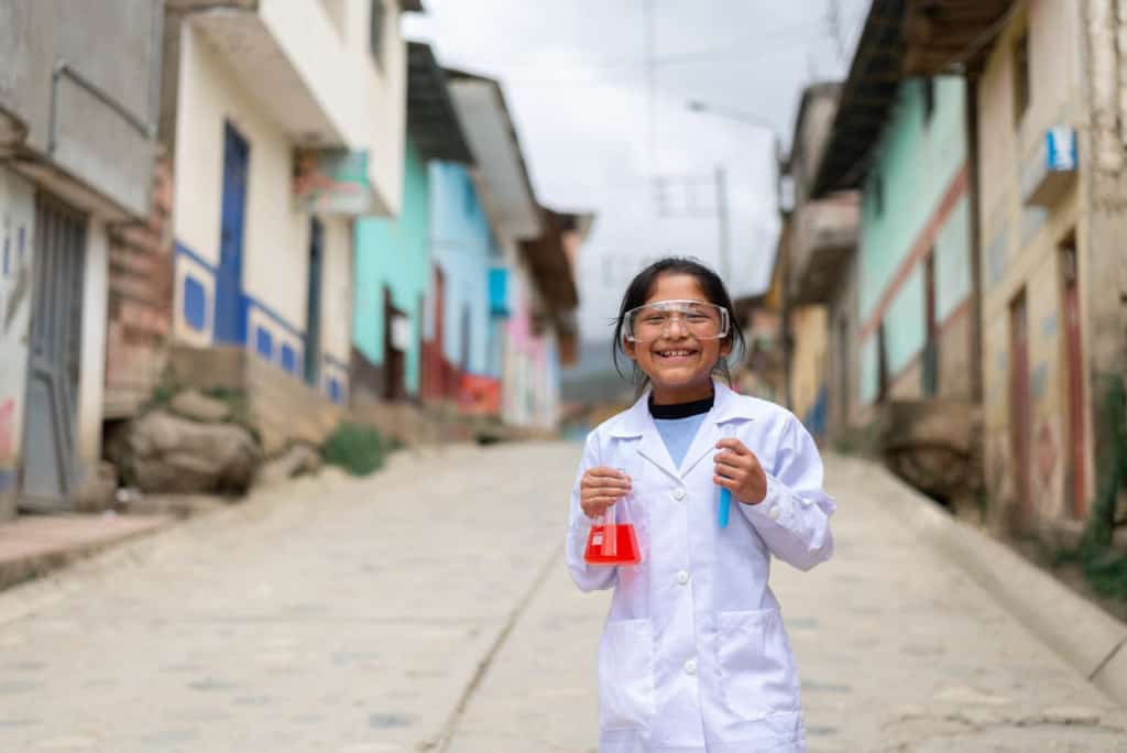 Girl wearing white scientist costume and holding test tubes in the streets of Huarichaca.