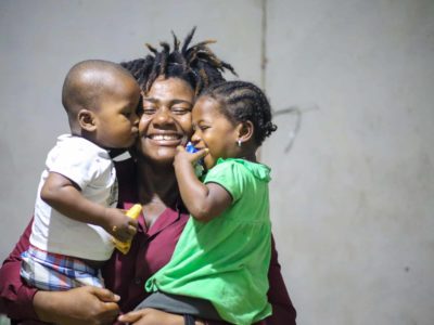 A Haitian woman smiles and holds her twin toddlers