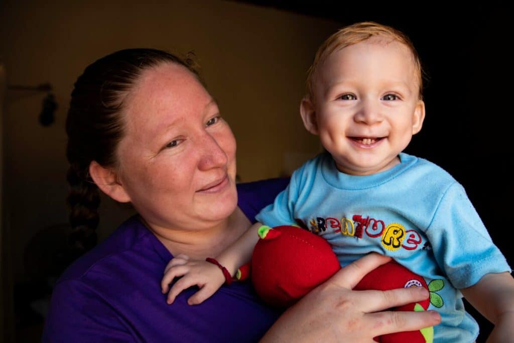 A strong mother in Honduras holds her baby, who is smiling and showing his dimples and bottom teeth.