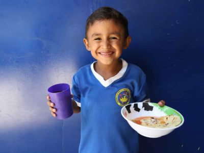 Boy wearing a blue shirt with white collar and the background is a blue wall of the kitchen’s front.