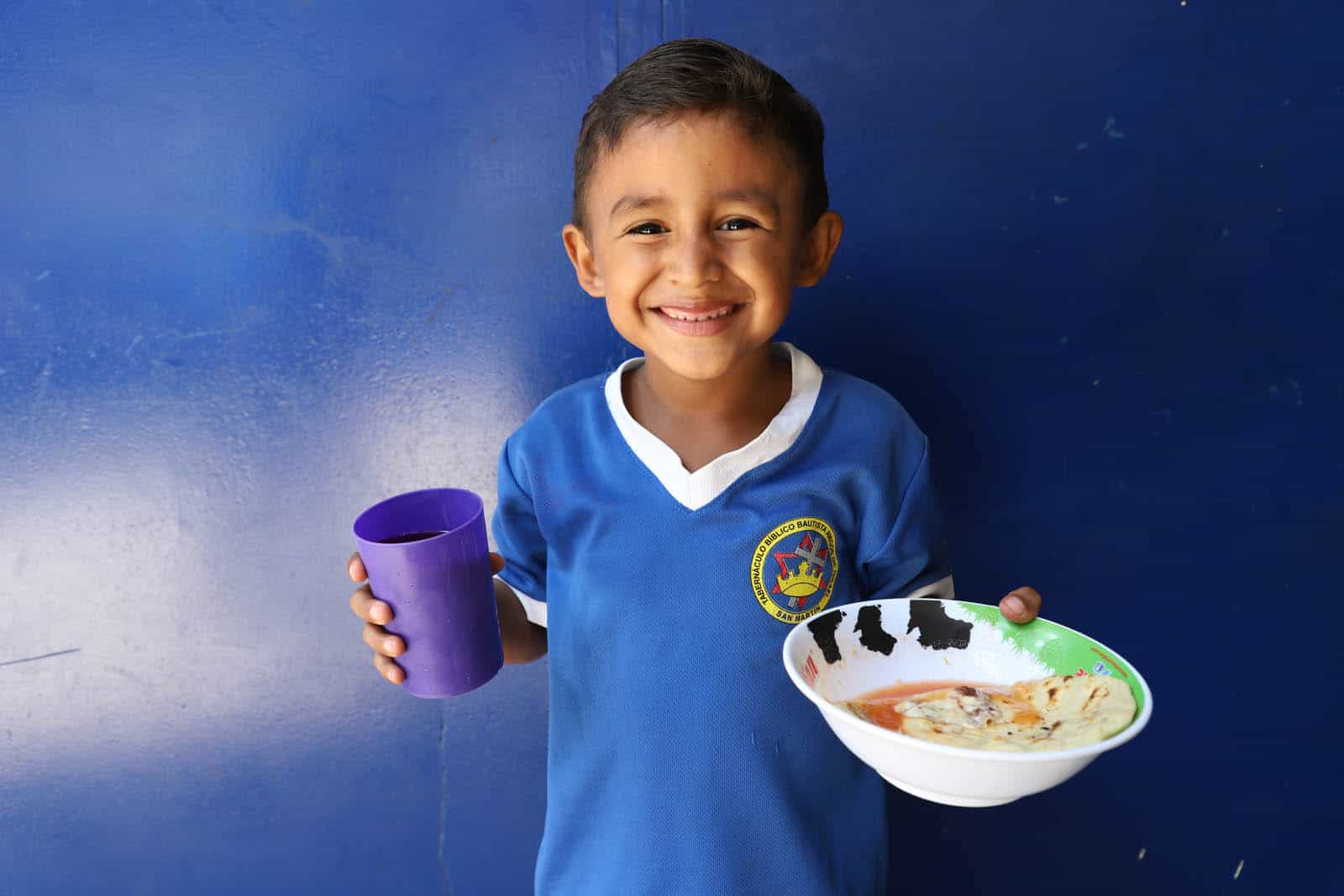 Boy wearing a blue shirt with white collar and the background is a blue wall of the kitchen’s front.