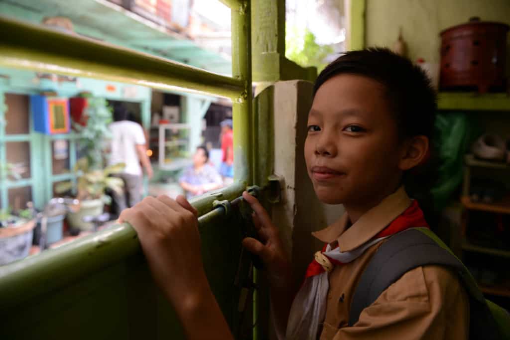 Boy in Jakarta smiles at the camera while wearing a tan shirt and backpack.