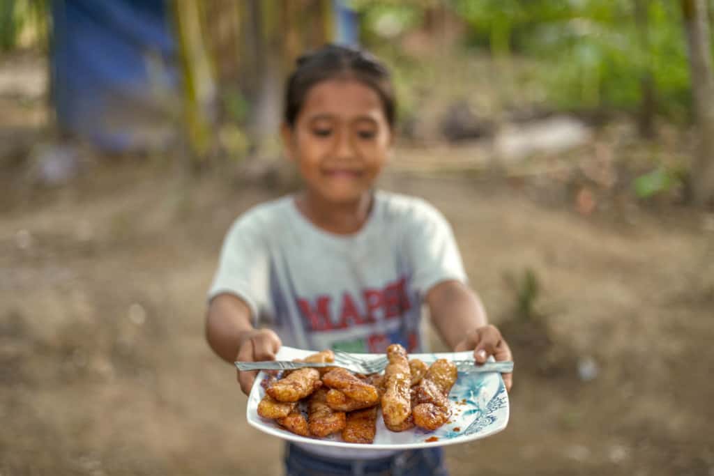Angel, in a gray shirt holds and looks at a white and blue plate of “buchi-buchi” in front of her. There is a fork on the plate.