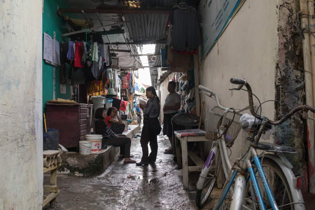 Two bicycles are leaning against a building in a narrow alley in ​​Pulomas, East Jakarta. Four people are in the alley, talking.