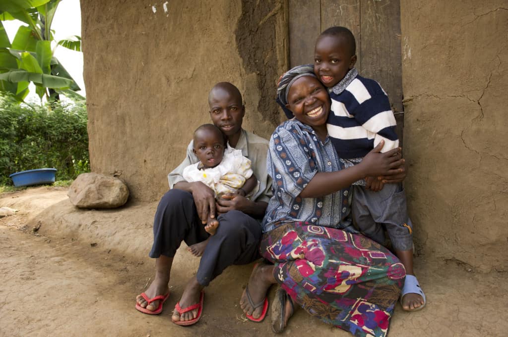 Hadija and her husband sit with their young son and daughter outside their mud home in Uganda