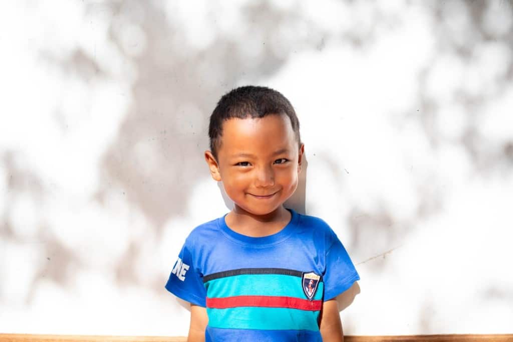 Weeview is wearing a blue shirt with black, green, and red stripes. He is standing in front of a white wall.