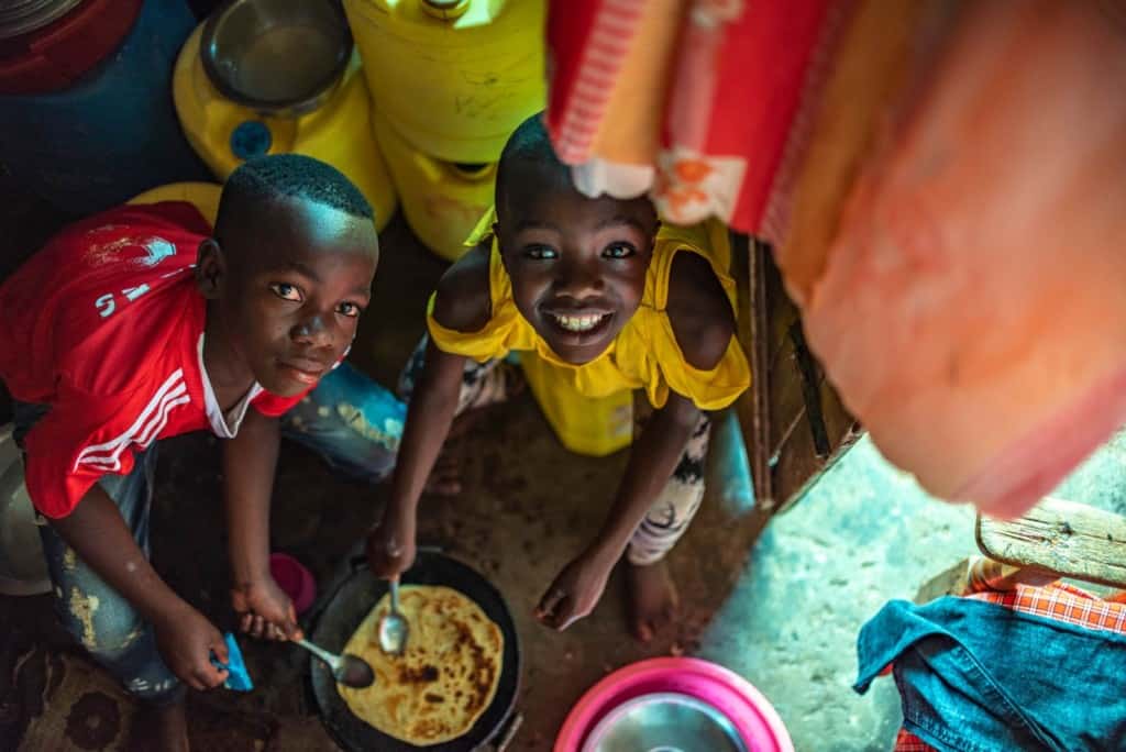 Leach and Moses are seen here helping to make Chapati, one of their favorite foods. They are looking up at the camera and smiling.