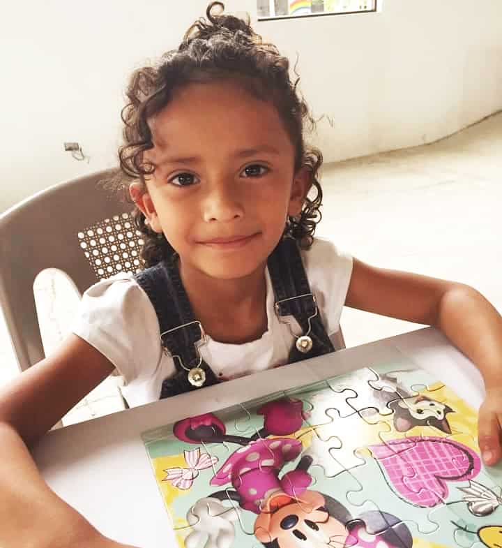 Genesis, a young girl with curly hair, sits by a completed Minnie Mouse puzzle.