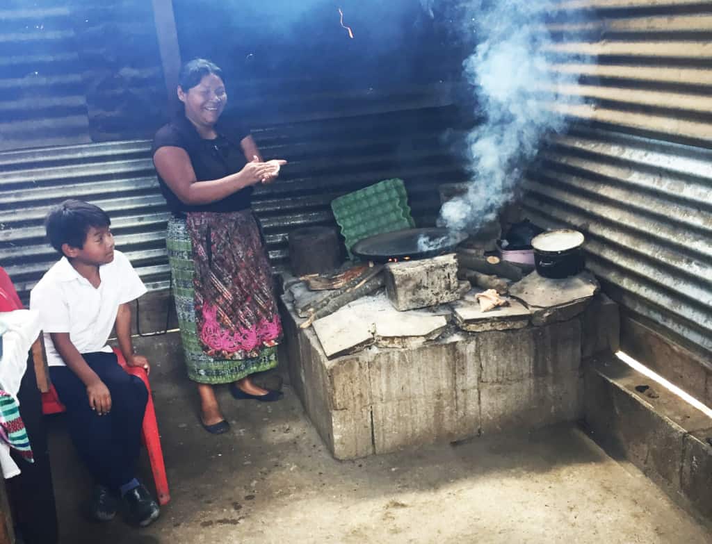 A mother wearing a black shirt and long skirt cooks in a Guatemalan kitchen.