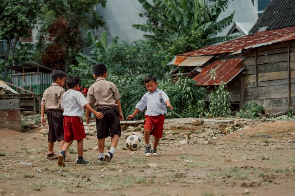 Boys race around the school playground kicking a soccer ball.