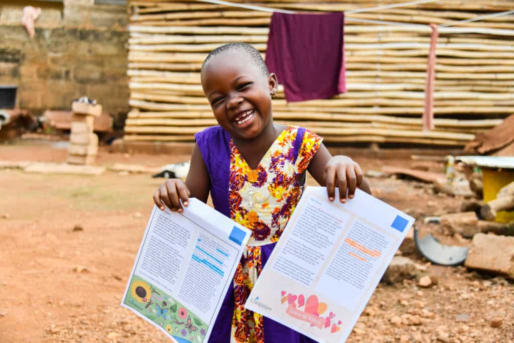 Fortune, a sponsored child in Togo, holds up letters from her sponsor. She is smiling and wearing a colorful dress.