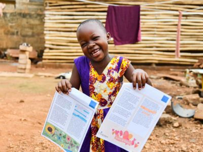 Fortune holds up letters from her sponsors. She is smiling and wearing a colorful dress.