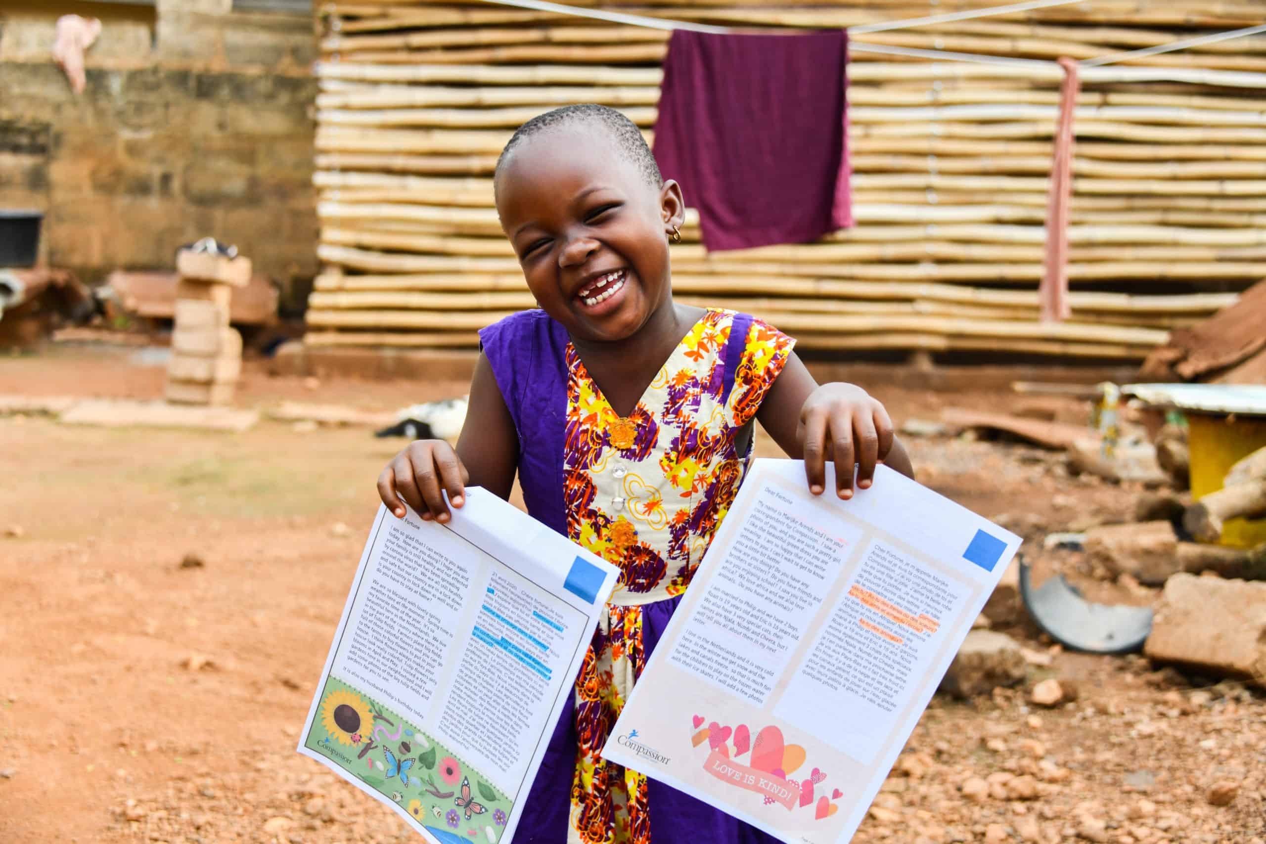Fortune holds up letters from her sponsors. She is smiling and wearing a colorful dress.