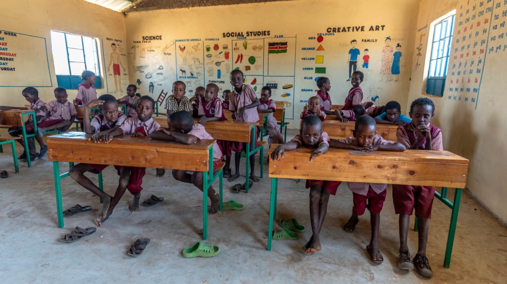 Children in a classroom sitting behind shared desks.