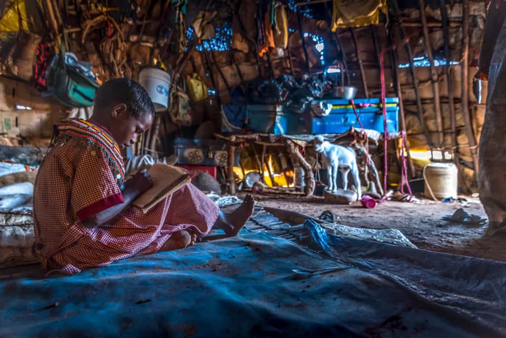 Maindi sits on the floor in her home and works on her homework.