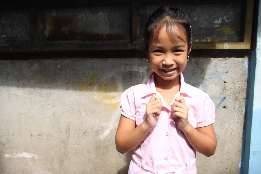 Girl standing outside her home, wearing her light pink dress she got for Christmas last year. She is holding onto the collar of the dress.