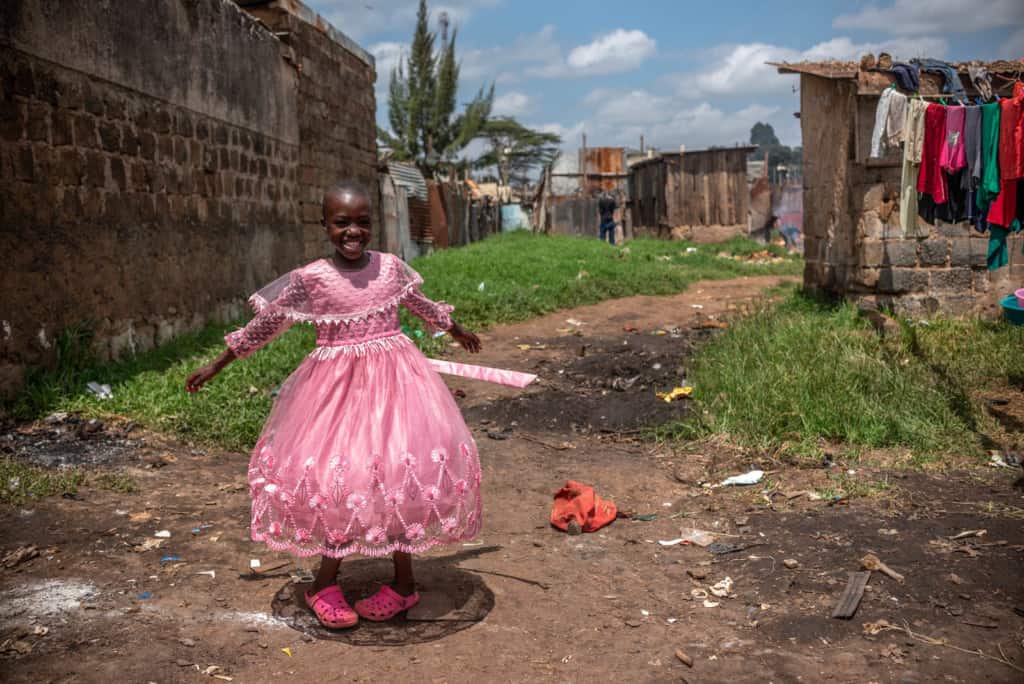 Leach is one of Kenya's girls. She is smiling and looking at the camera as she is wearing her pink dress and shoes.