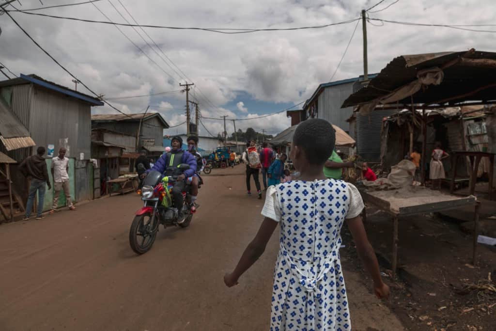 Gaudencia is wearing a white dress with a blue pattern. She is walking through the streets which are full of people. 