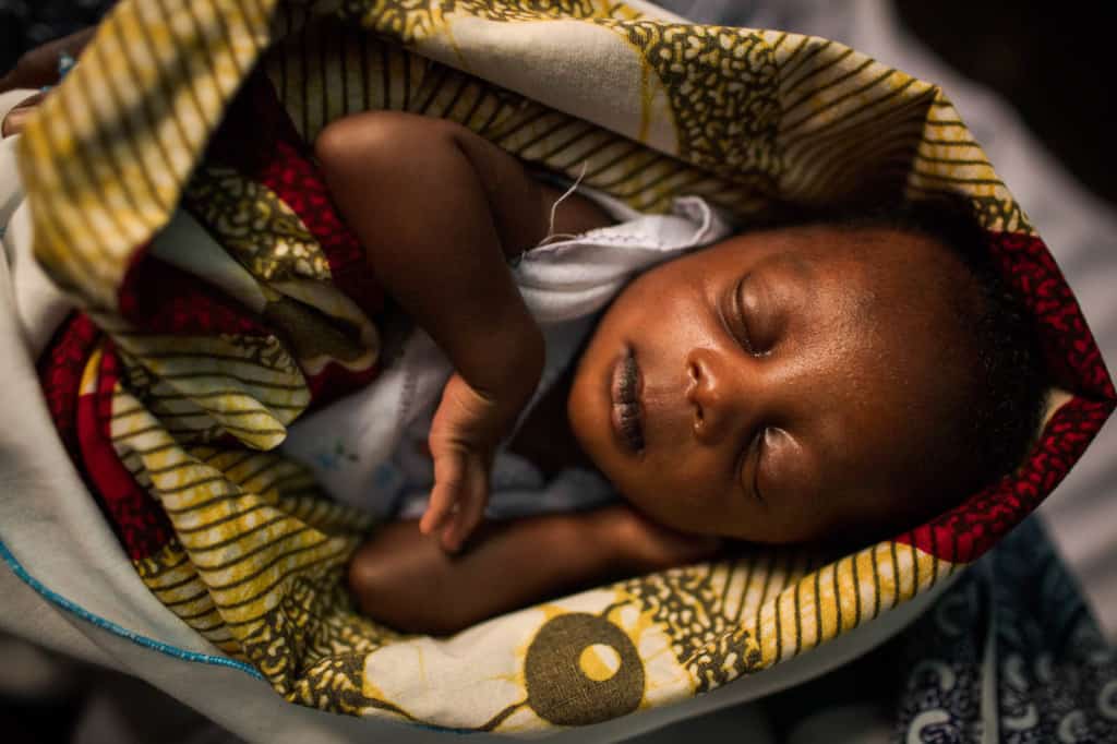 A sleeping baby girl is wrapped in a red and yellow blanket.