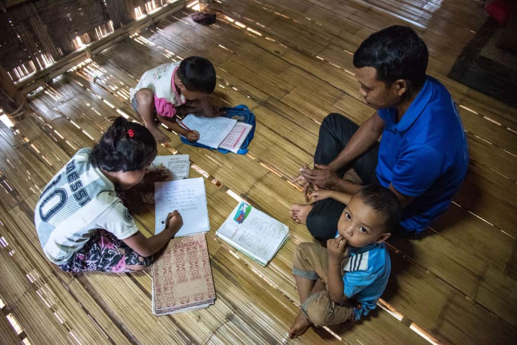 Karmaly's father is on the floor of their home helping with her homework.