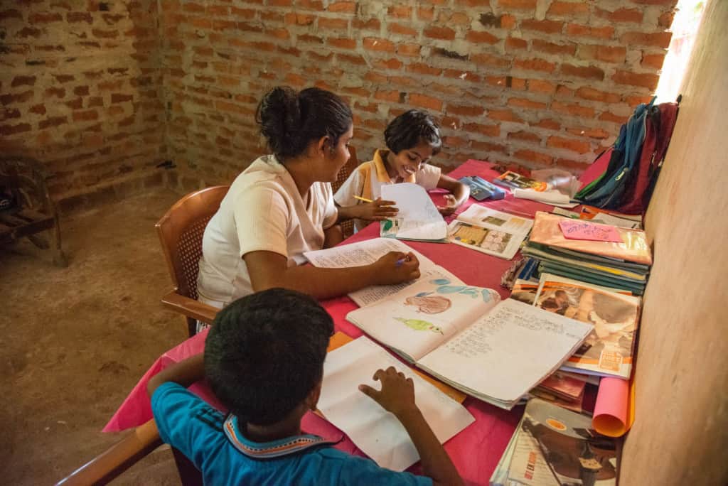 The children are sitting at  a table working on their homework. There are brick walls behind them.