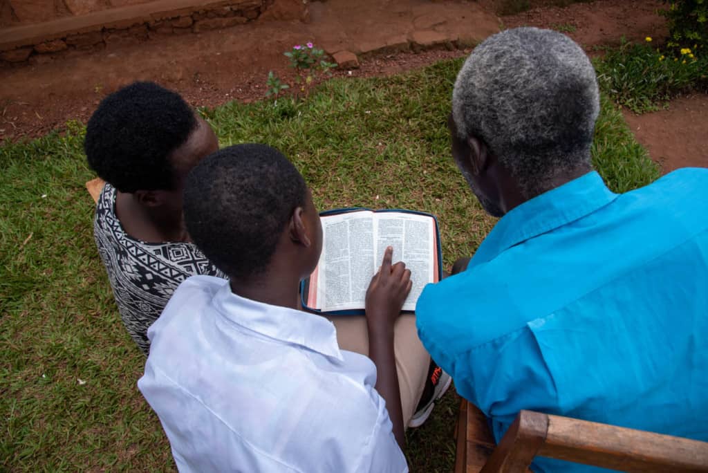 Daughter, father and mother in front of their house reading a Bible.