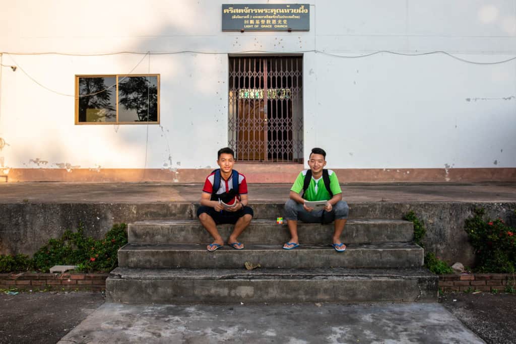 Sirasak and Chaiweera are sitting in front of a white Church building where they both always hang out during a break between Thai school and Chinese school.