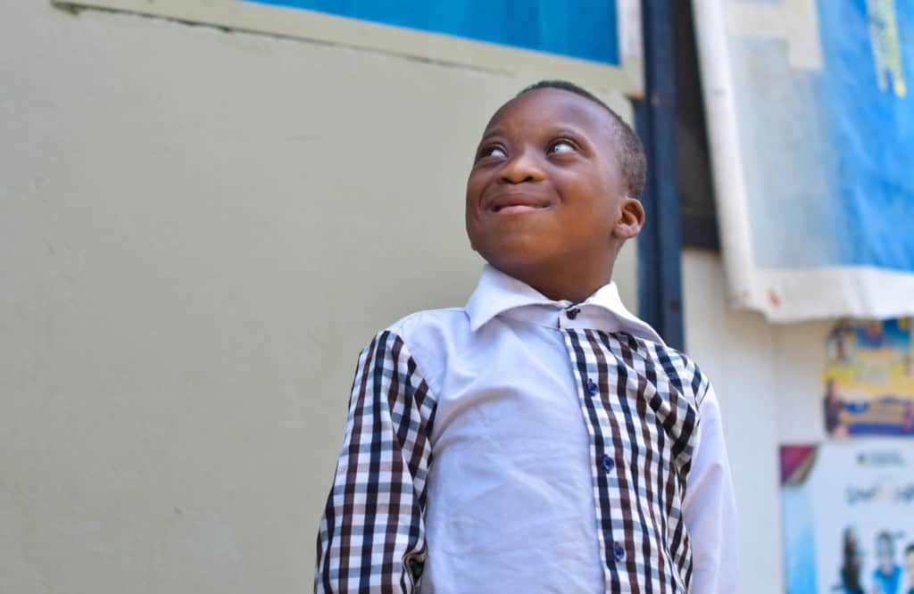 Wisdom, a boy who lives in poverty with disabilities, smiles. He wears a black and white button-down shirt.