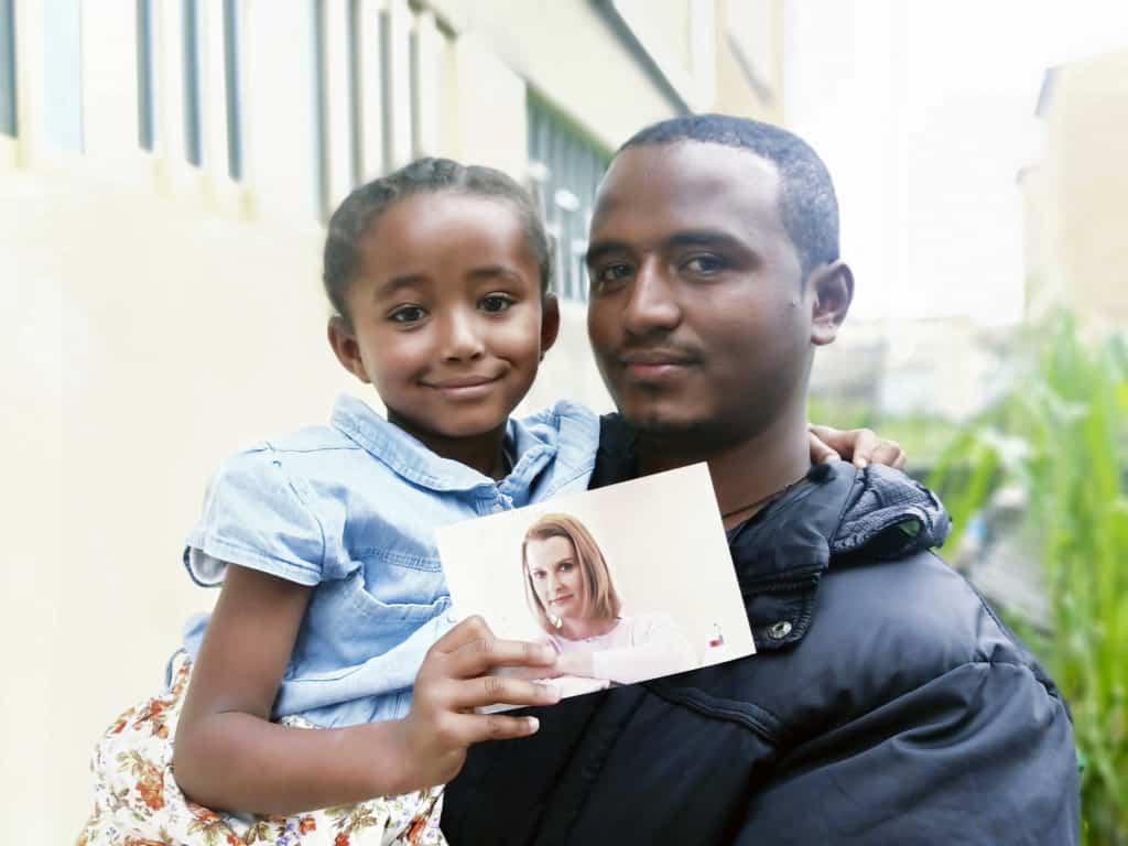 Sintayehu is holding his daughter Lisa, who is holding a photo of her father's former sponsor