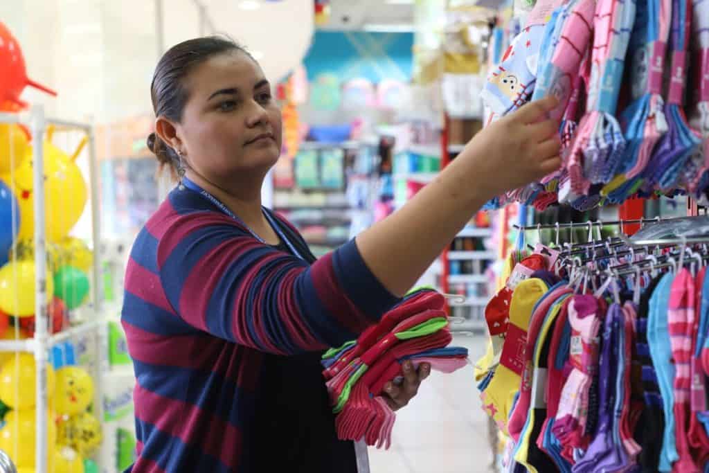 A woman wearing a maroon and blue cardigan is shopping for baby clothes at a store in El Salvador.