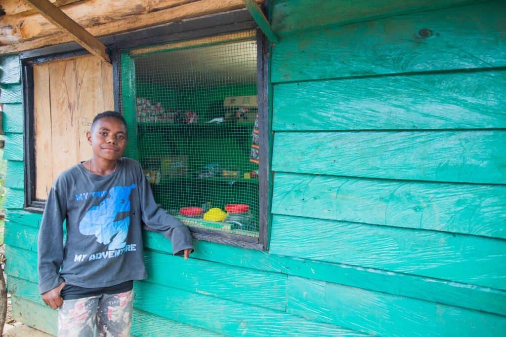 A teenage boy stands outside a shop window in Indonesia. The shop is painted teal green. 