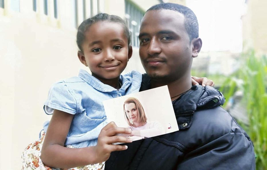 A father holds his daughter, who is holding a photo of a woman