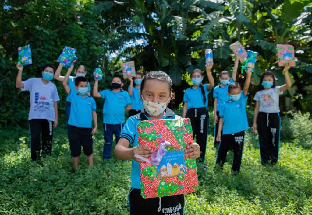 A group of sponsored children are showing their wrapped Christmas presents. Everyone wears face masks and uses social distancing to avoid COVID-19 spread.