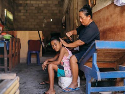 A mother brushes a daughter's hair. They are inside their home.