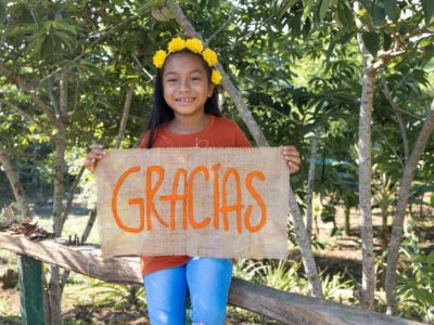Maira in Colombia holds a sign that says Gracias, Spanish for thank you. She is thankful for her sponsor and her family's food farm.
