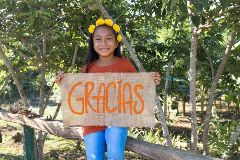 Maira in Colombia holds a sign that says Gracias, Spanish for thank you. She is thankful for her sponsor and her family's food farm.