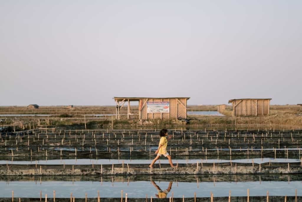 A girl walks along a salt pond. Her father is a salt farmer in Indonesia.