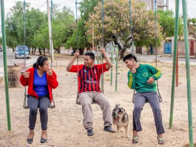 A father and his two children swing on a swing set in Bolivia. A dog is with them.
