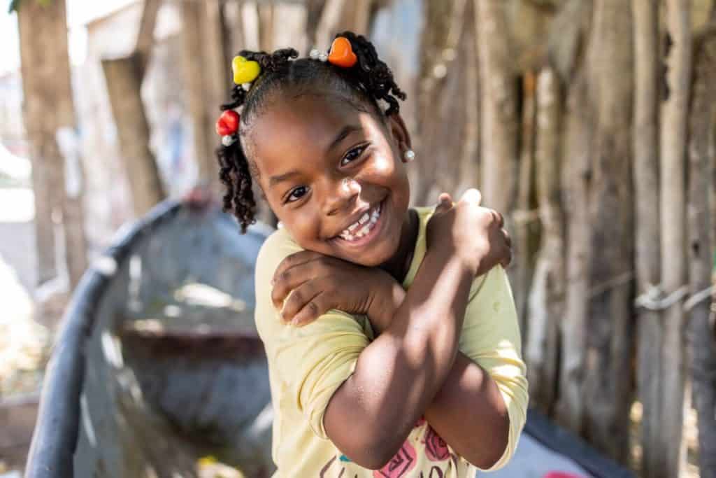 Zahen is wearing a yellow shirt. She is sitting in a boat on the seashore giving herself a hug.