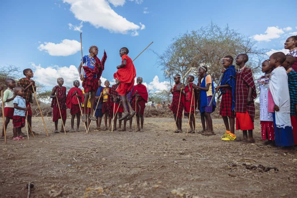 A group of Maasai people are outside singing and dancing together in celebration.