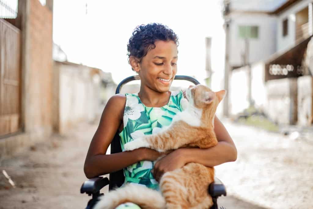 Kauany poses with her new cat Nino. She is sitting in her wheelchair outside, and is looking down at her cat.