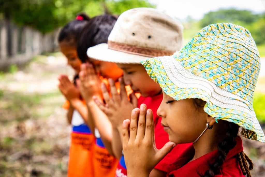 Girls pray together. They are standing outside with their hands folded in front of their faces.