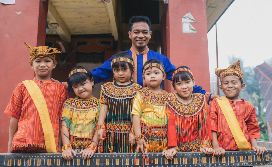 A pastor stands outside a church in Indonesia with children wearing traditional clothing