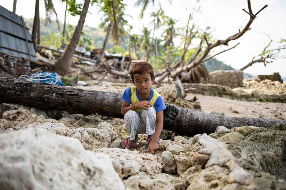 A boy wearing a blue and yellow shirt sits among wood and rocks in the Philippines.