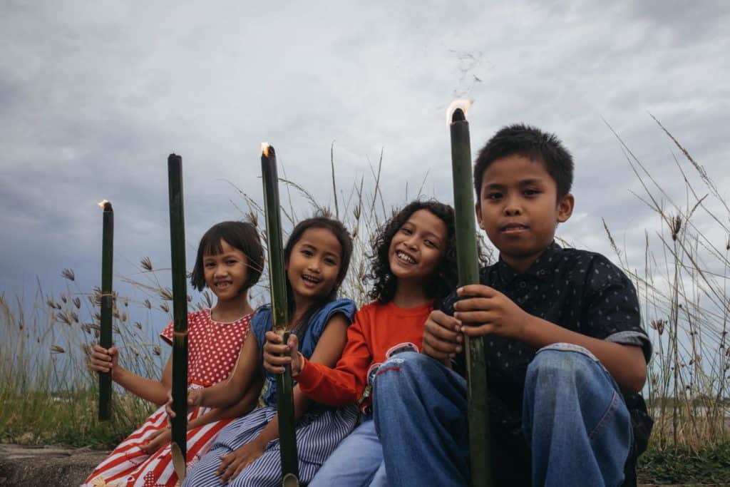 Four friends are sitting outside together,  each of them holding a burning bamboo torch.