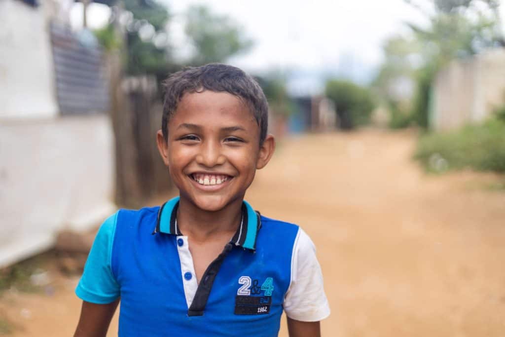 Boy wearing a blue shirt and is standing outside his home.