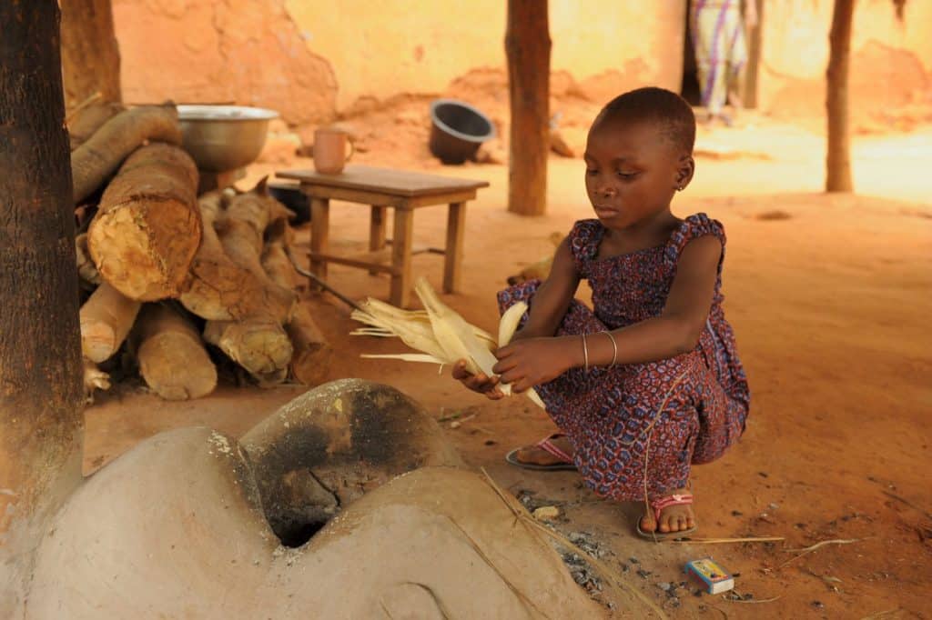 Girl squatting by a fire holding a corn husk.