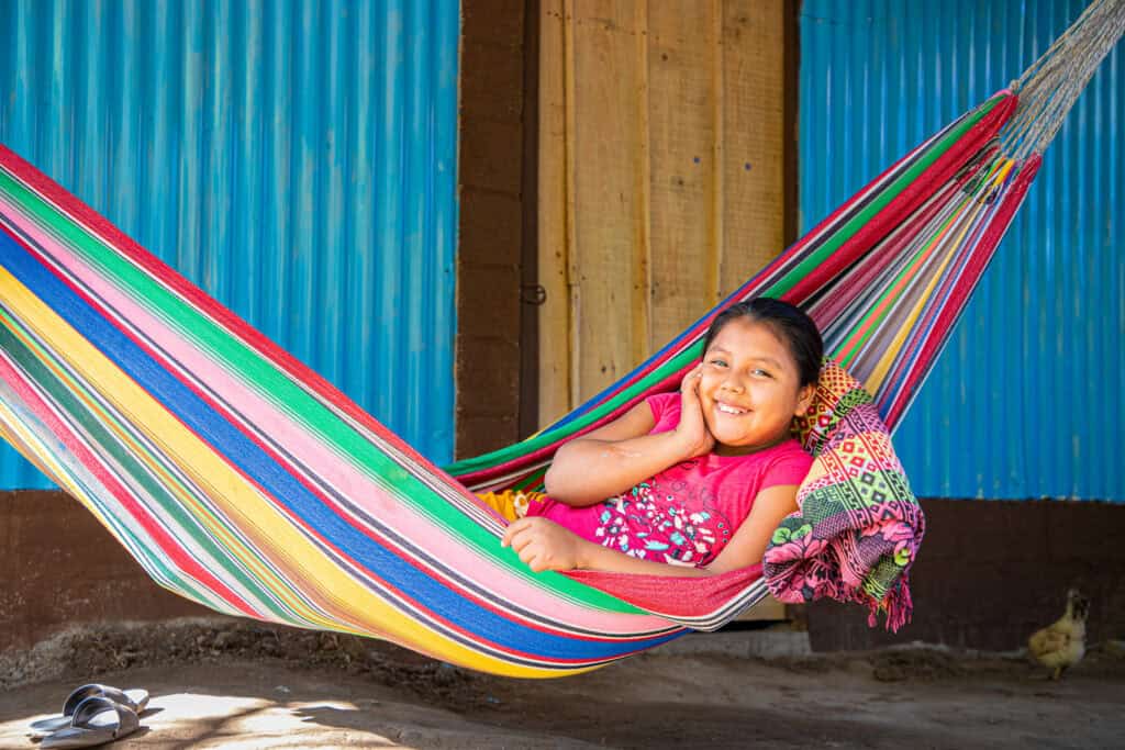 Young girl lies in a brightly colored hammock and smiles at the camera
